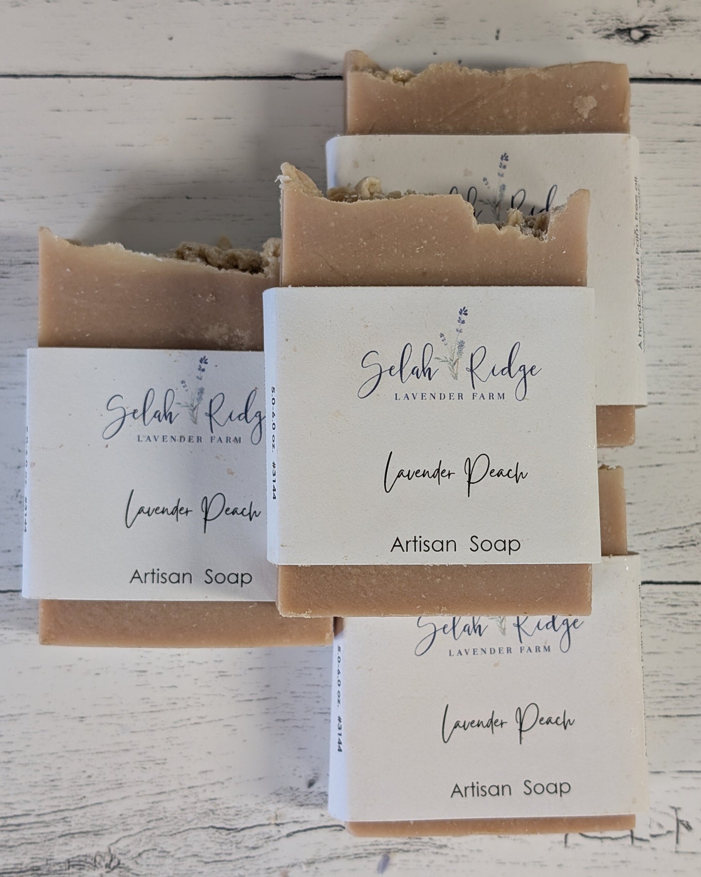 Three bars of lavender peach artisan soap with visible labels on a wooden surface