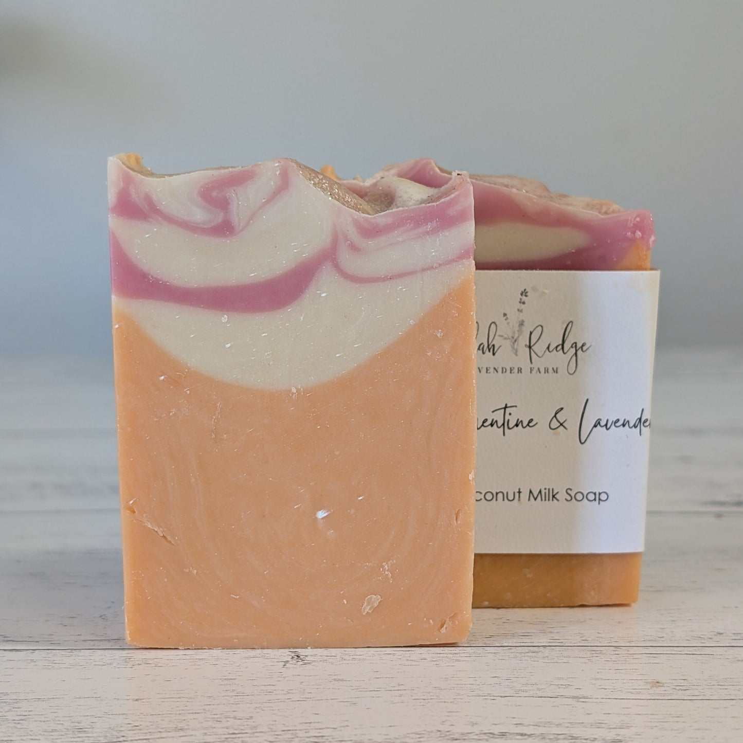 Bar of soap with pink and white swirls next to a label on a wooden surface